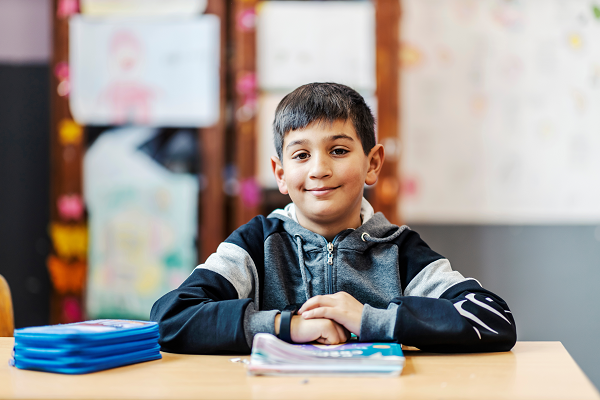 A Roma boy is in a classroom sitting by his desk