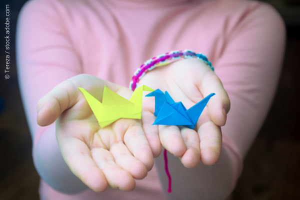 A person holding in her hands a yellow and a blue origami 