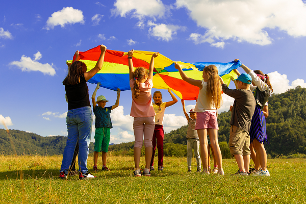A group of children are on a field and hold together a colorful flag