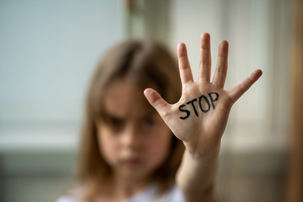 Child raising hand, on which is written 'STOP'