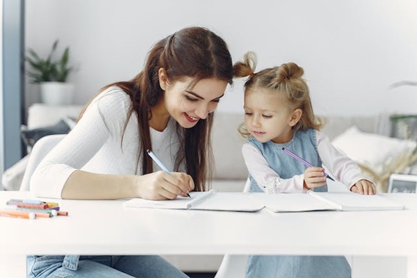 A woman showing a young child to write on a notepad