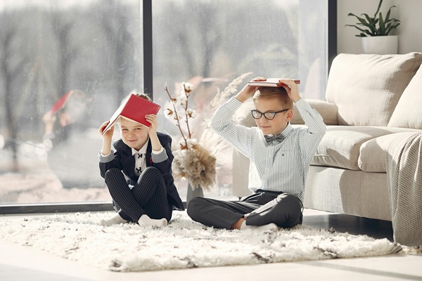 Two children sitting on floor with books on their heads