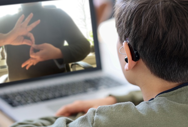 Deaf teenager wearing hearing aid using laptop