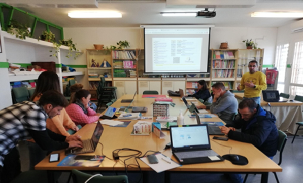 Students around a table with laptoips looking at a presentation on a screen