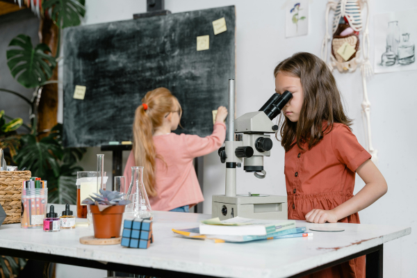 two students in a classroom: One using a microscope, the other wriiting on the blackboard