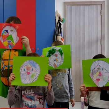 Four children holding up abstract art work depicting their faces in front of their face.