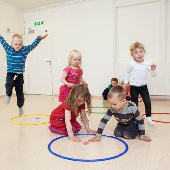 Photo of kindergarten children playing a core PTLM game. Two children are visiting a hoop with a letter in it. Other children are travelling to the hoop. They are all engaged in the game.