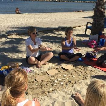 A very relaxing image of teachers sat in a circle under the palm trees on the beach practising mindful techniques.