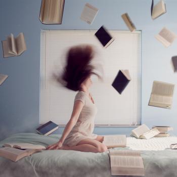 A woman sitting on a bed with books in the air