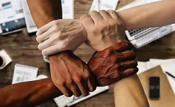 Four hands of different ethnicities crossed and holding each other for a wrist