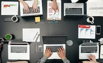 Hands working on laptops on a desk from above 