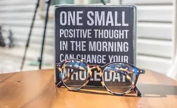 Glasses on the desk in front of a tile with positive psychology statement