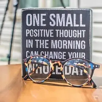 Glasses on the desk in front of a tile with positive psychology statement