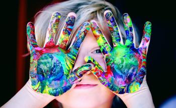 A face of a child behind hands covered in paint 