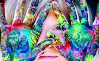 A face of a child behind hands covered in paint 