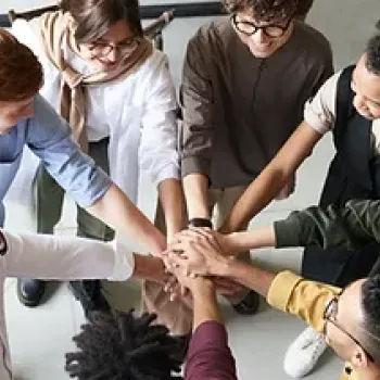 People standing in a circle and with one hand each on top of all the other hands in the middle