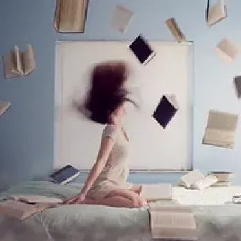 A woman sitting on a bed with books in the air
