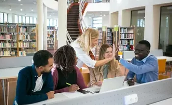 People sitting at a desk in a library and one person giving high-five to another