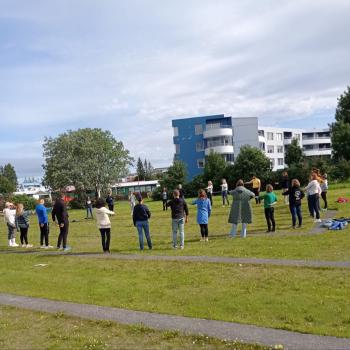 Group of participants engaging in an outdoor classroom activity in a lush green field under clear skies with modern buildings in the background.
