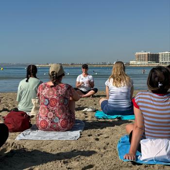 A group of our participants enjoying a mindfulness session on the beach with clear blue sea in the background