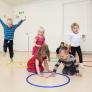 Photo of kindergarten children playing a core PTLM game.  Two children are visiting a hoop with a letter in it.  Other children are travelling to the hoop. The are all engaged in the game.