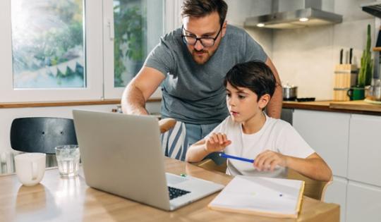 Father helping son with schoolwork on laptop
