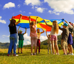 A group of children are on a field and hold together a colorful flag