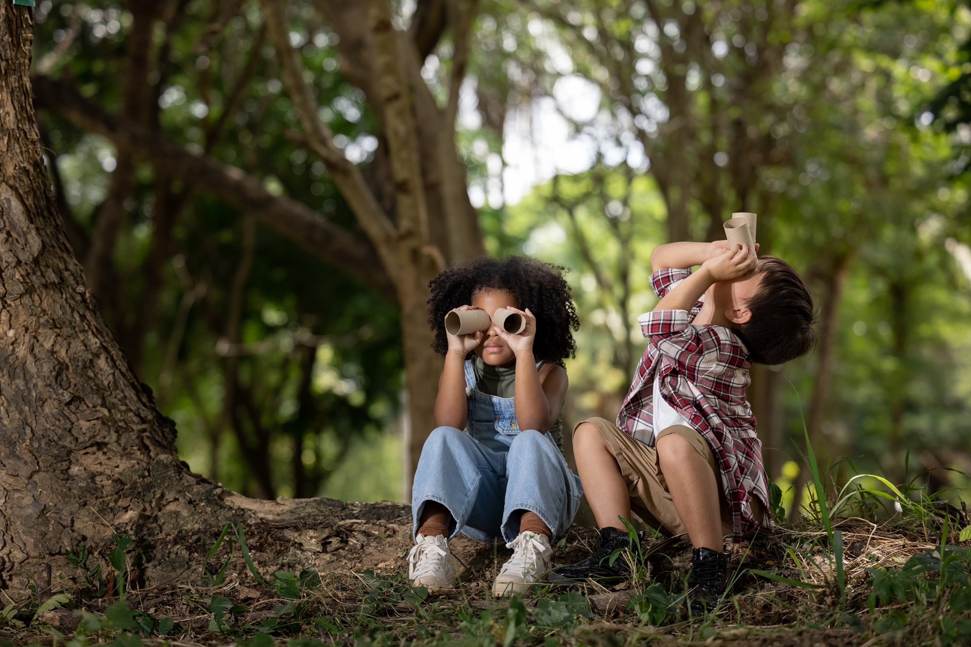 Children sitting in the woods and using playing using binoculars
