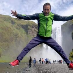 Teacher jumping for joy in front of a the beautiful Icelandic waterfall Seljalandsfoss.