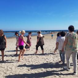 A group of teachers taking part in a well-being movement activity on the beach. They are walking barefoot with the sea in the background.