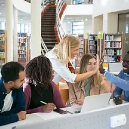 People sitting at a desk in a library and one person giving high-five to another