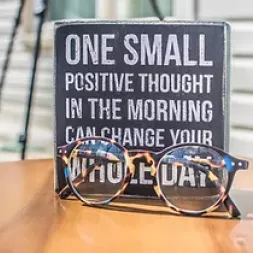 Glasses on the desk in front of a tile with positive psychology statement