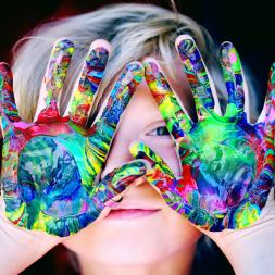 A face of a child behind hands covered in paint