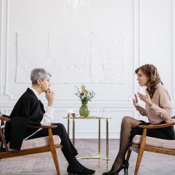 2 women sitting opposite, one is explaining, one is listening