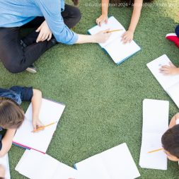 students and teacher writing on the grass